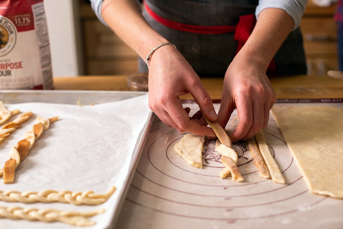 A baker twisting two strips of pie dough together to make a cinnamon-sugar twist