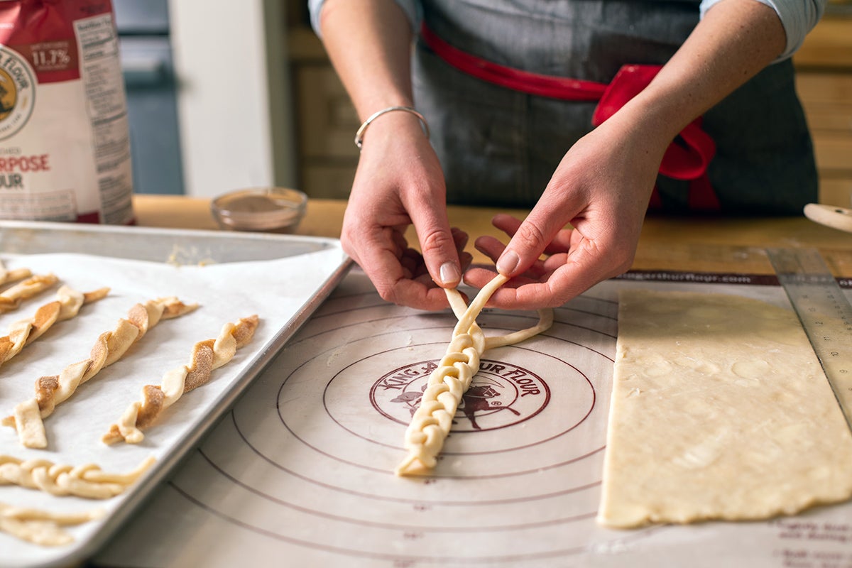 A baker braiding three strips of pie dough to decorate the top of a custard pie