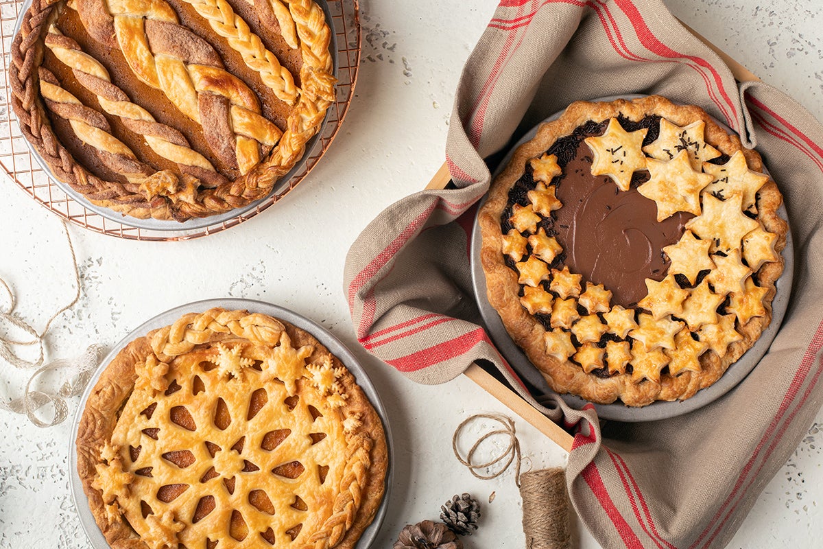 Three custard pies on a table, ready for sharing: chocolate cream, pumpkin pie, and lemon chess