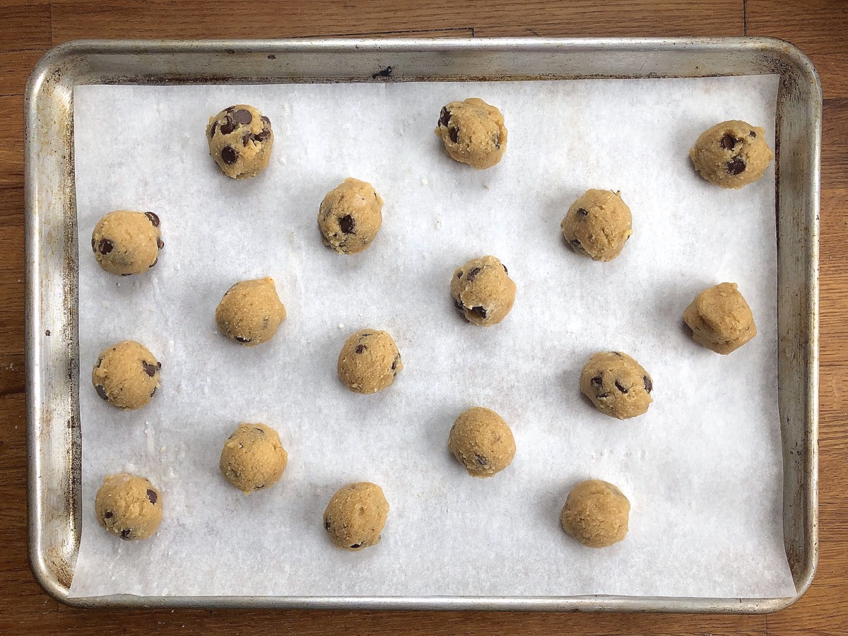 Dough for Gluten-Free Almond Flour Chocolate Chip Cookies scooped into balls on  a parchment-lined baking sheet.