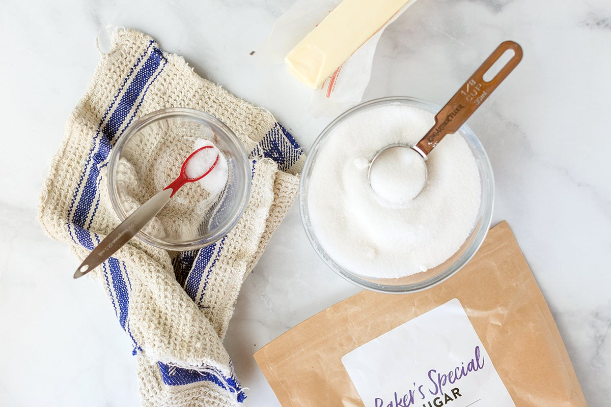 A bowl of superfine sugar and a small ramekin of salt with a measuring spoon on a kitchen table