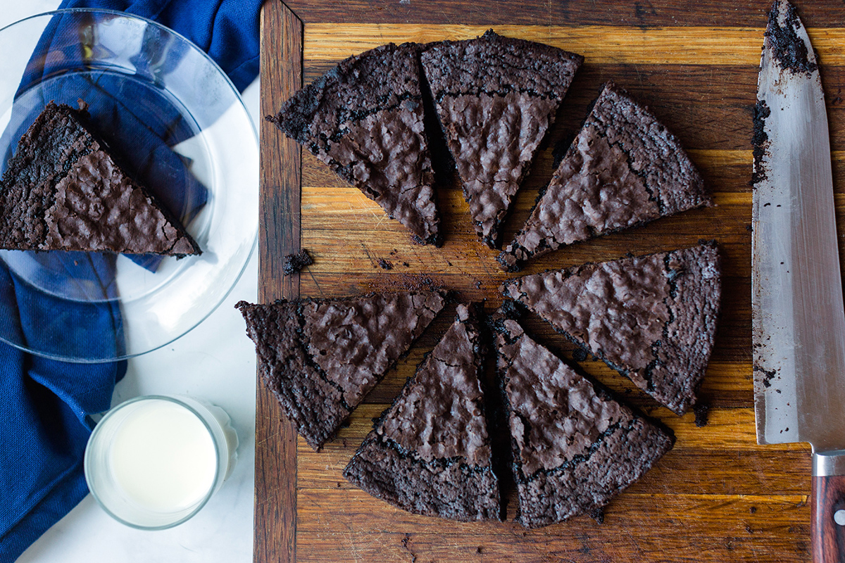 Gluten-free brownies baked in a round cake pan, sliced into wedges, with a glass of milk