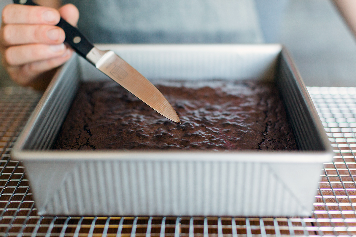 A baker inserting a paring knife into a pan of freshly baked gluten-free brownies to see if they're done