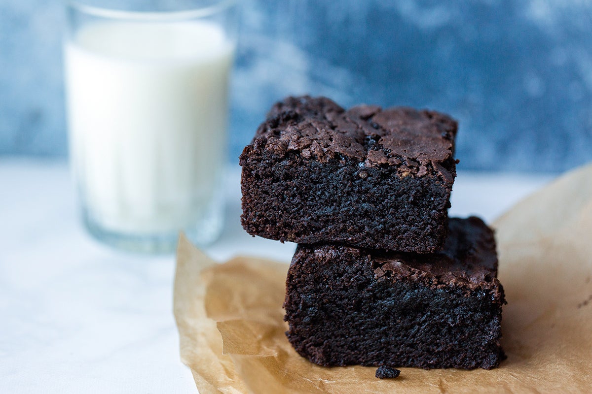 Two gluten-free brownies stacked on top of each other with a glass of milk