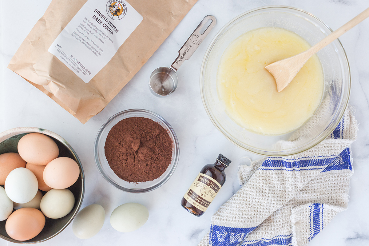 Ingredients for making gluten-free brownies, including melted butter sugar, cocoa powder, and eggs
