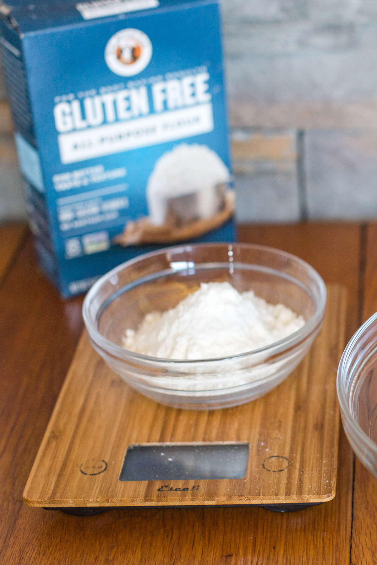 A bowl of gluten-free flour on a scale with a box of gluten-free flour in the background