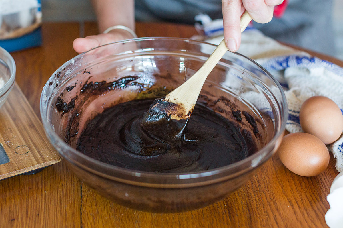 A baker mixing gluten-free brownie batter and adding eggs, one at a time