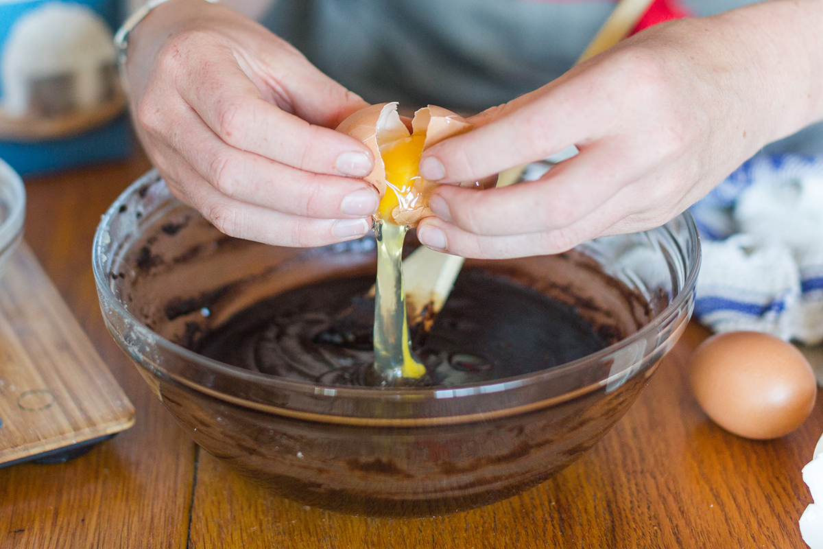 A baker cracking an egg into a bowl of gluten-free brownie batter