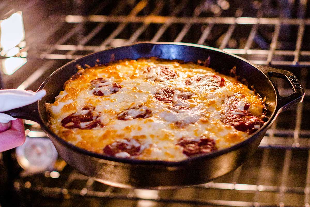 A baker removing a Gluten-Free Pan Pizza from the oven that looks golden brown on top