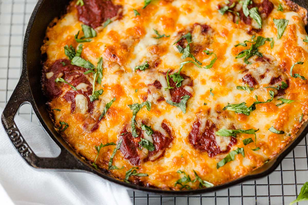 A close up shot of Gluten-Free Pan Pizza in a cast iron pan showing off the crispy edges