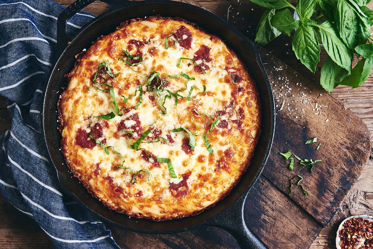 Gluten-Free Pan Pizza topped with cheese, sauce, and fresh basil in a cast iron pan