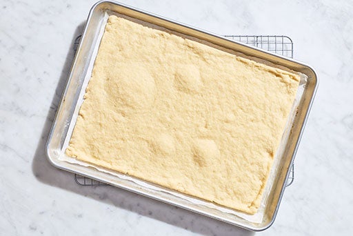 Parbaked gluten-free pizza dough on a rectangular sheet tray.