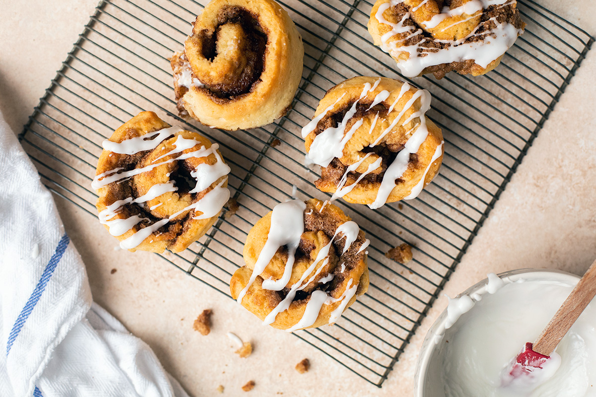 Freshly baked gluten-free cinnamon rolls drizzled with glaze on a cooling rack