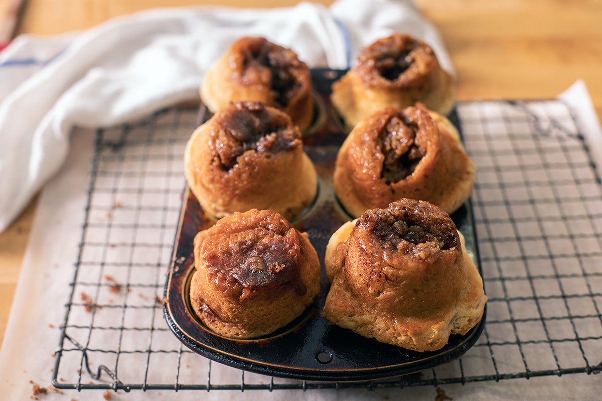 Freshly baked gluten-free cinnamon rolls cooling upside down on a cooling rack, showing off the sticky bottom