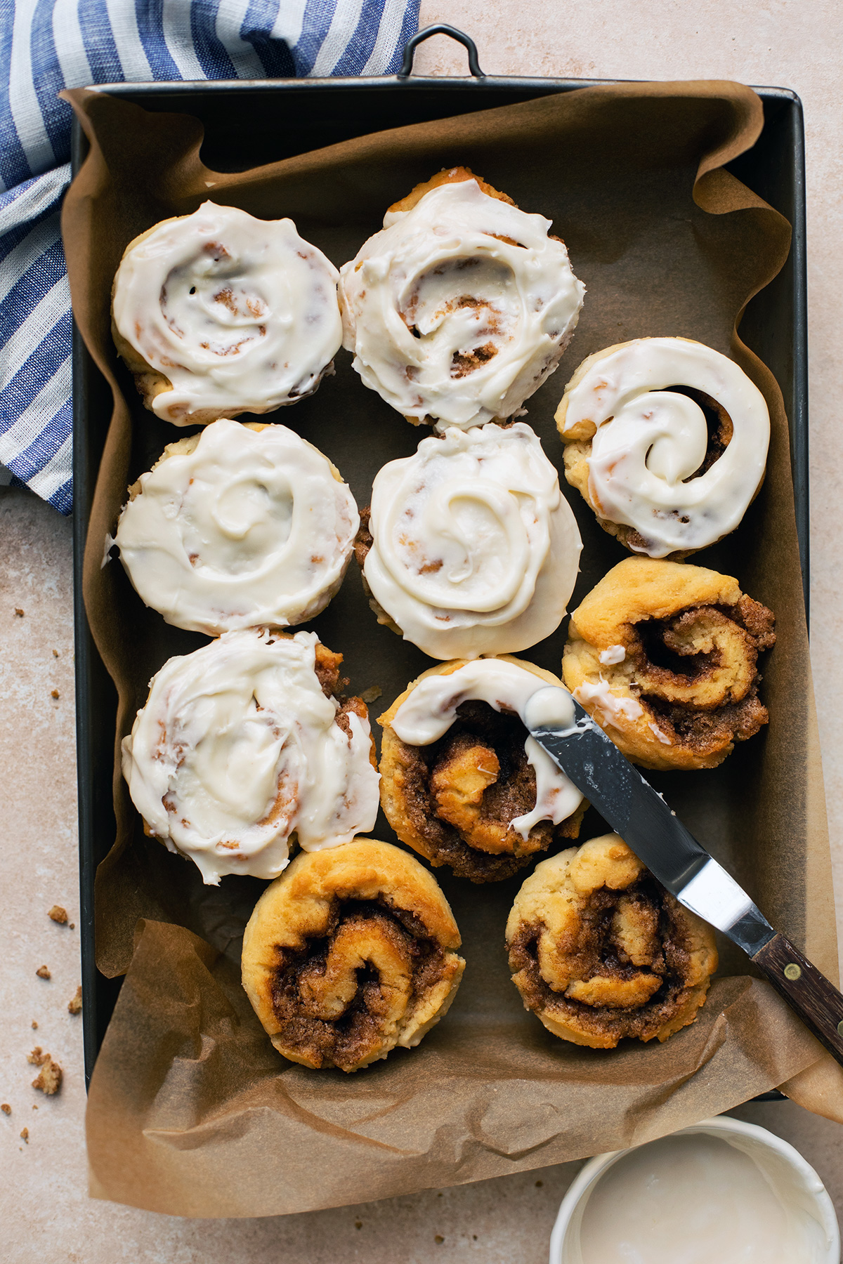 A tray of gluten-free cinnamon rolls, half covered with cream cheese frosting