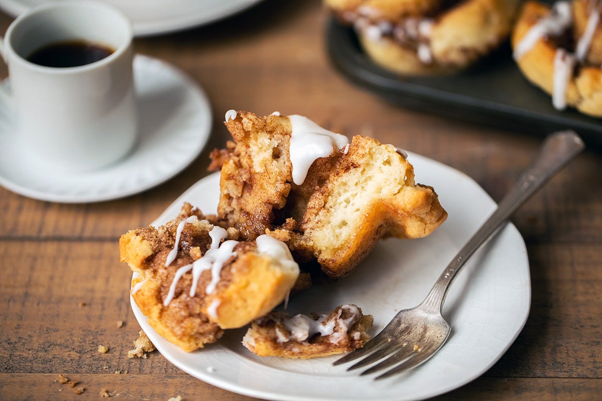 A gluten-free cinnamon roll on a small plate, split in half and covered with frosting