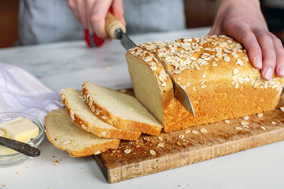 A baker slicing a loaf of gluten-free sandwich bread on a cutting board