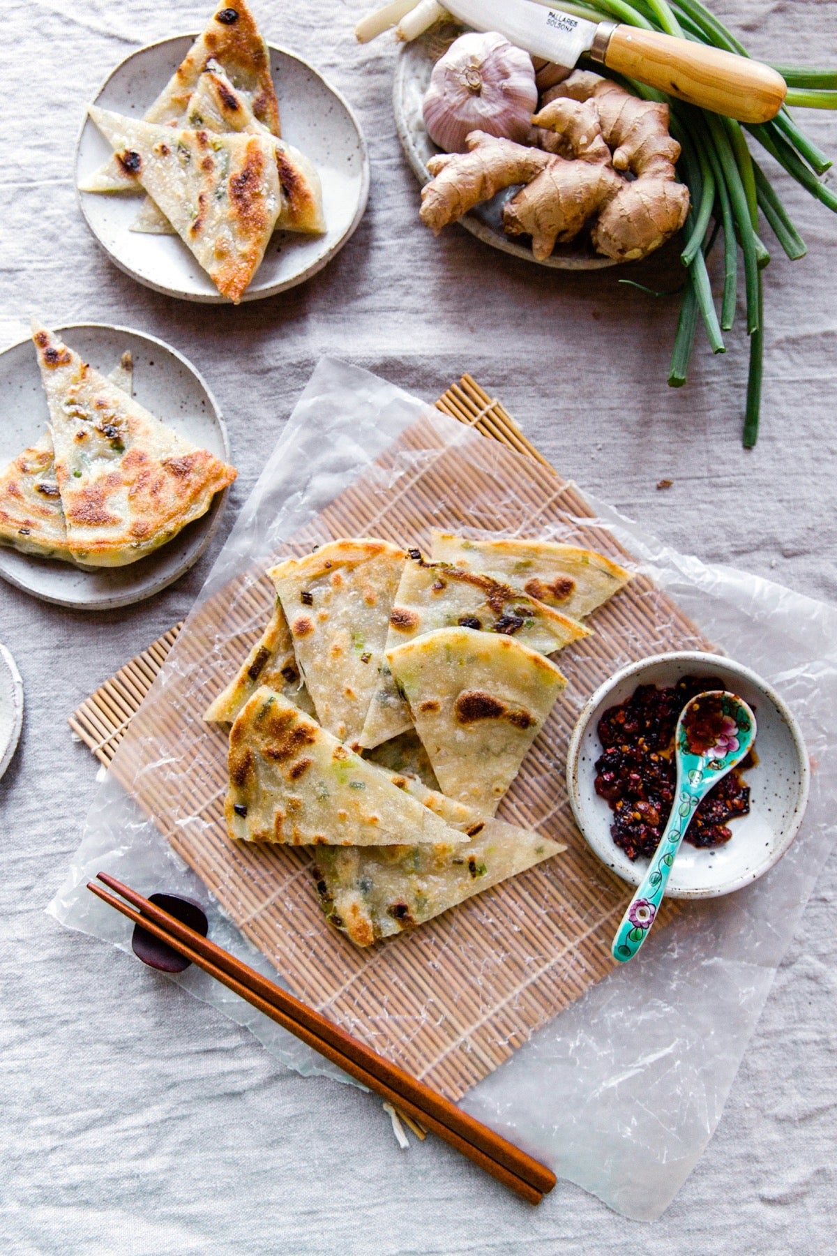 Scallion pancakes with dipping sauce, on a serving mat with chopsticks.