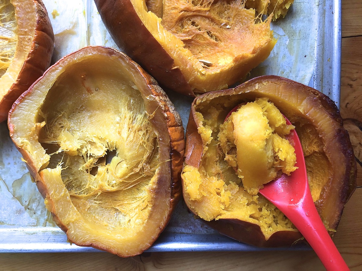 Roasted pumpkin halves on a baking sheet, their flesh being spooned out.