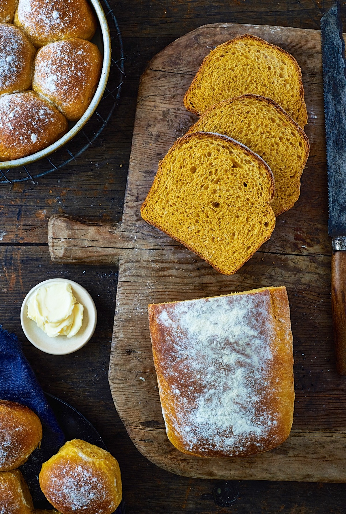 Pumpkin yeast bread on a cutting board, sliced, flanked by pumpkin yeast rolls.