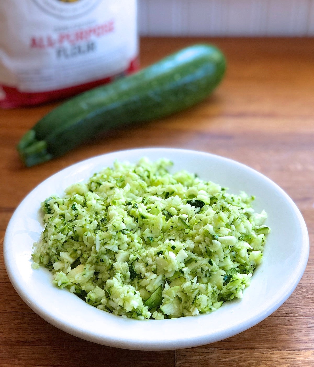 Whole zucchini with a bowl of chopped aucchini.