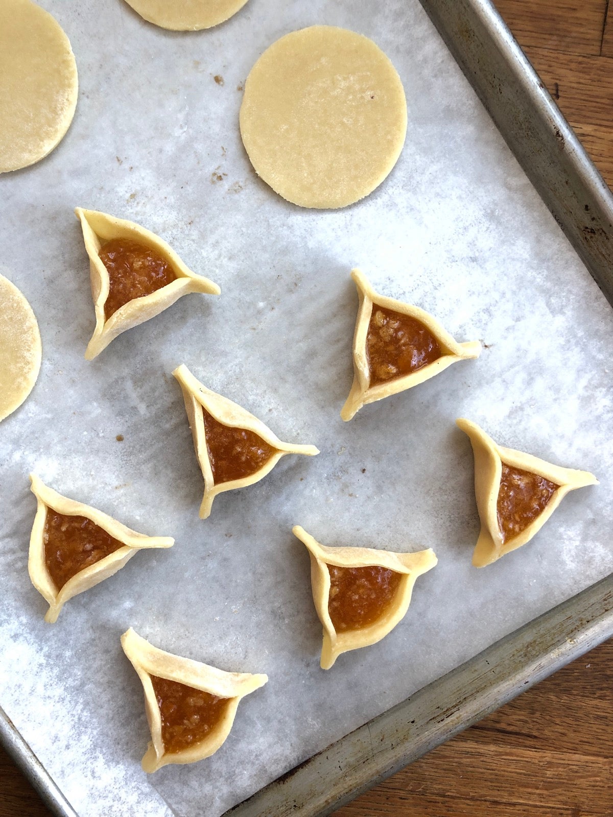 Showing how to fill and shape Hamantaschen dough: first the circle of dough, then a dollop of filling in the middle, then one side folded up, then the other two sides folded.