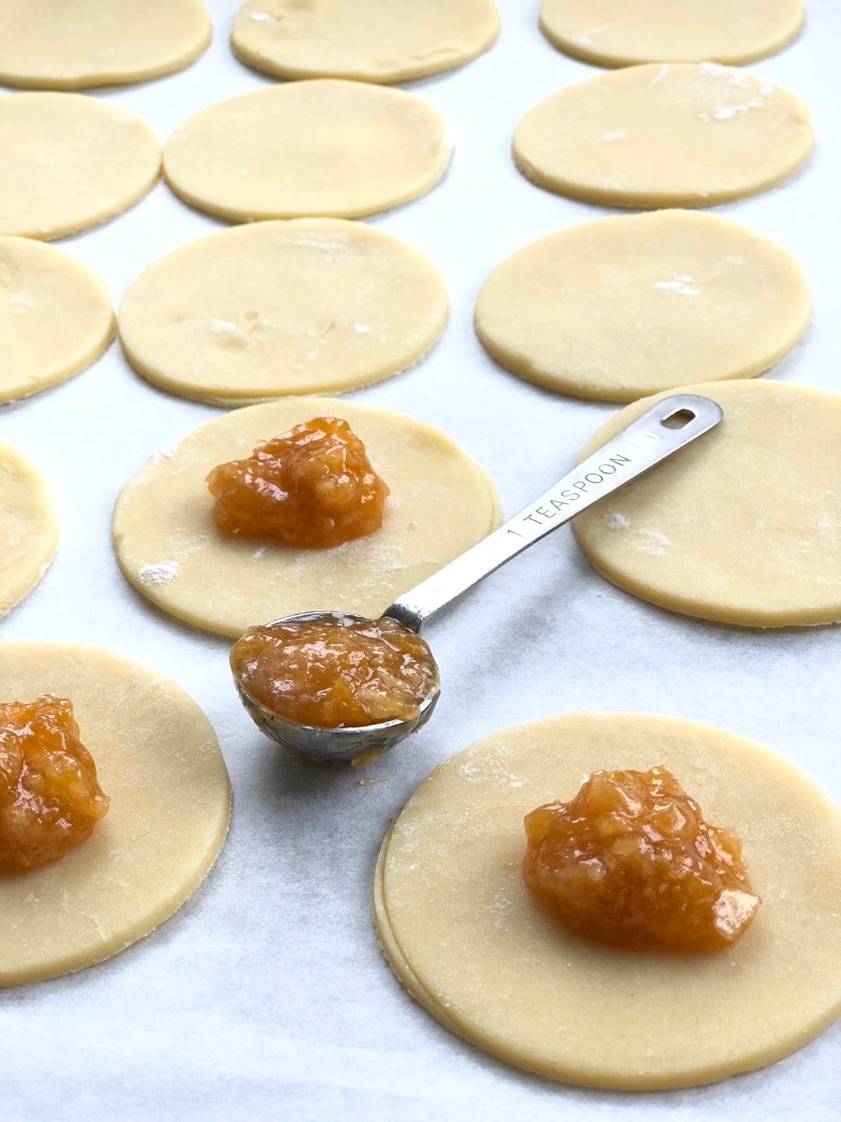 Rounded measuring teaspoonful of apricot filling, ready to top a round of cookie dough.