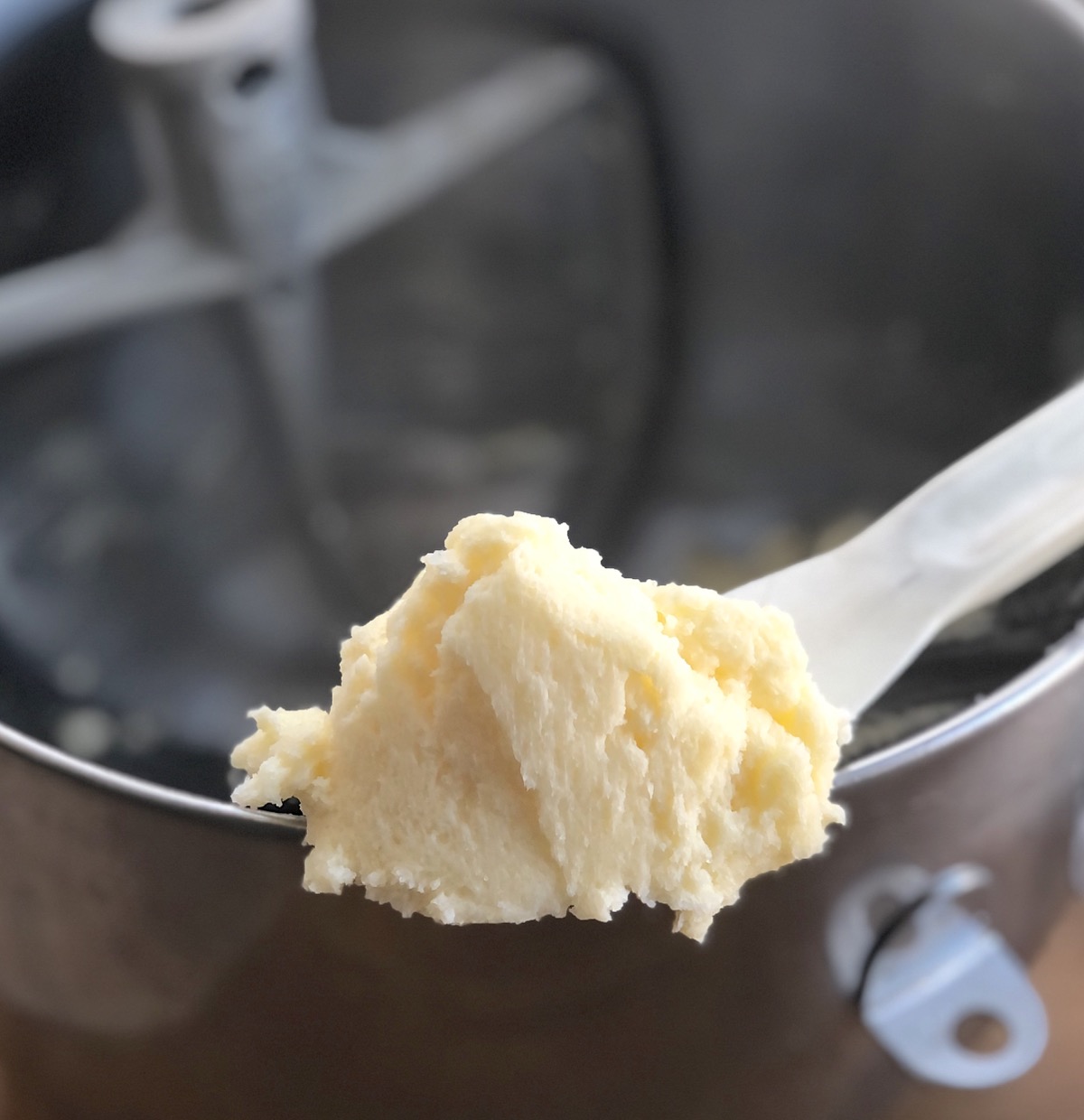A dollop of butter and sugar beaten until light and fluffy, shown on a spatula above a mixing bowl.