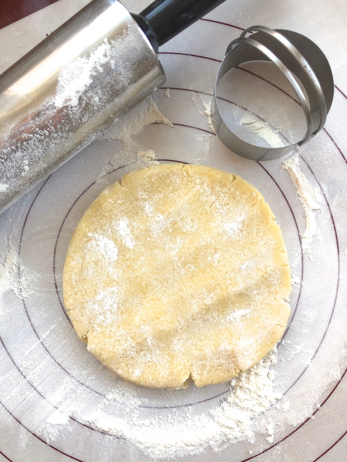 Disc of dough on a silicone rolling mat, rolling pin on the side, dough gently tapped to soften and flatten it a bit.