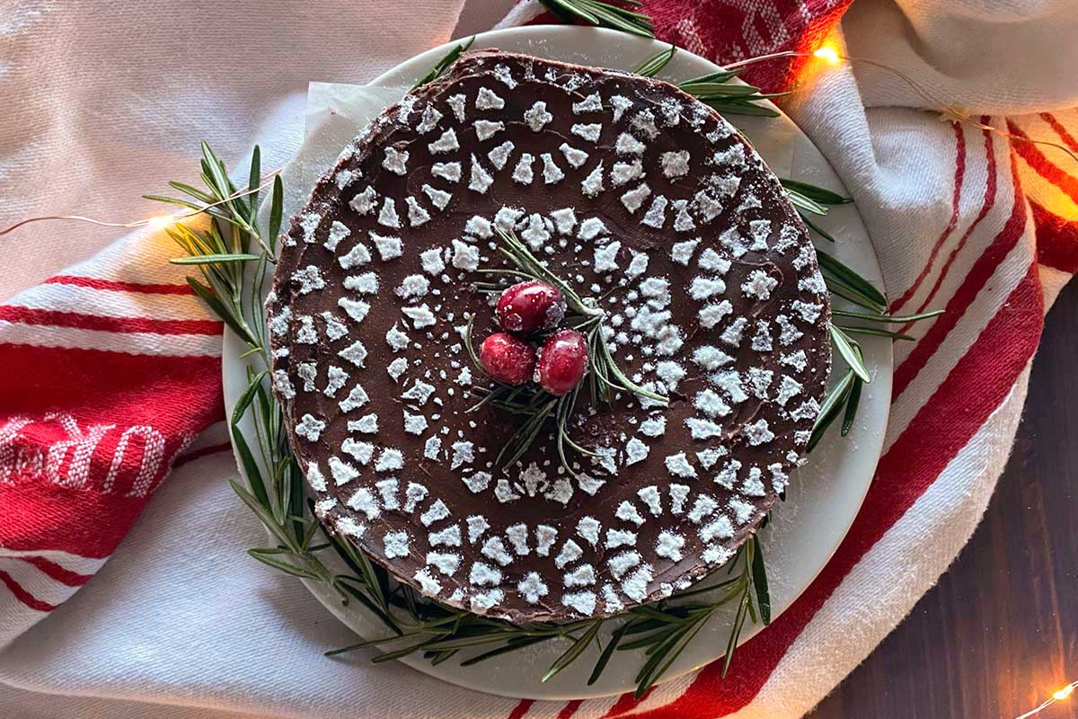 A flourless chocolate cake with an intricate design stenciled on top using confectioners' sugar