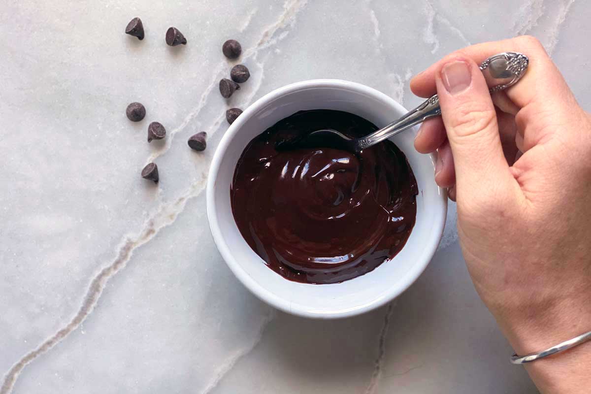 A small bowl of chocolate ganche next to a few chocolate chips