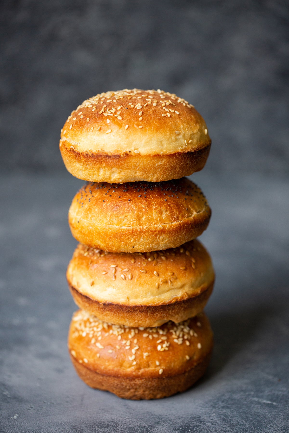 Una pila de cuatro bollos de hamburguesa caseros cubiertos con semillas