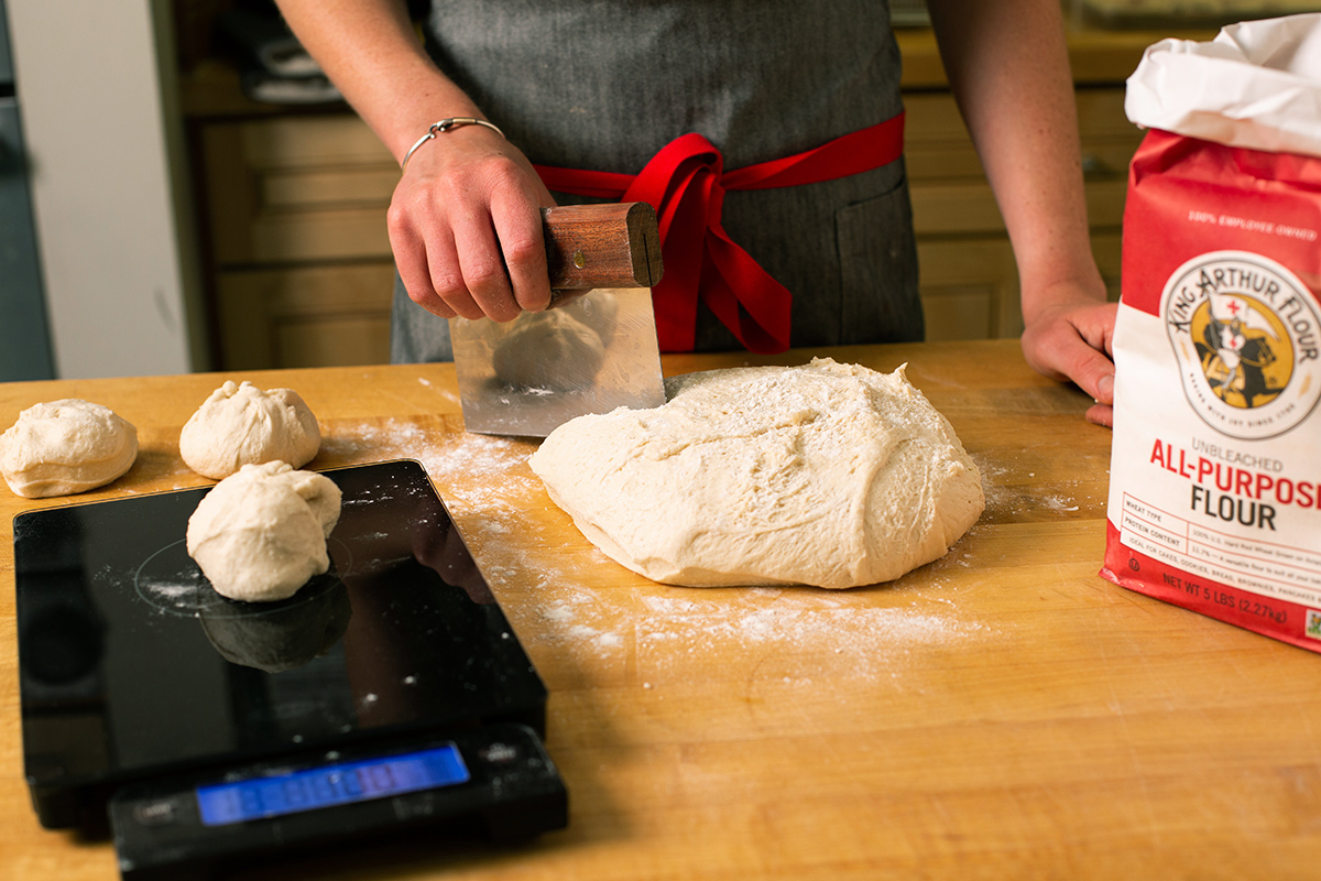 A baker dividing hamburger bun dough into pieces and weighing them on a scale