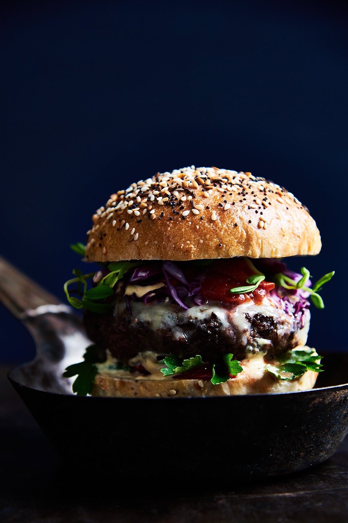 A burger on a homemade bun topped with vegetables and condiments in a small cast iron pan