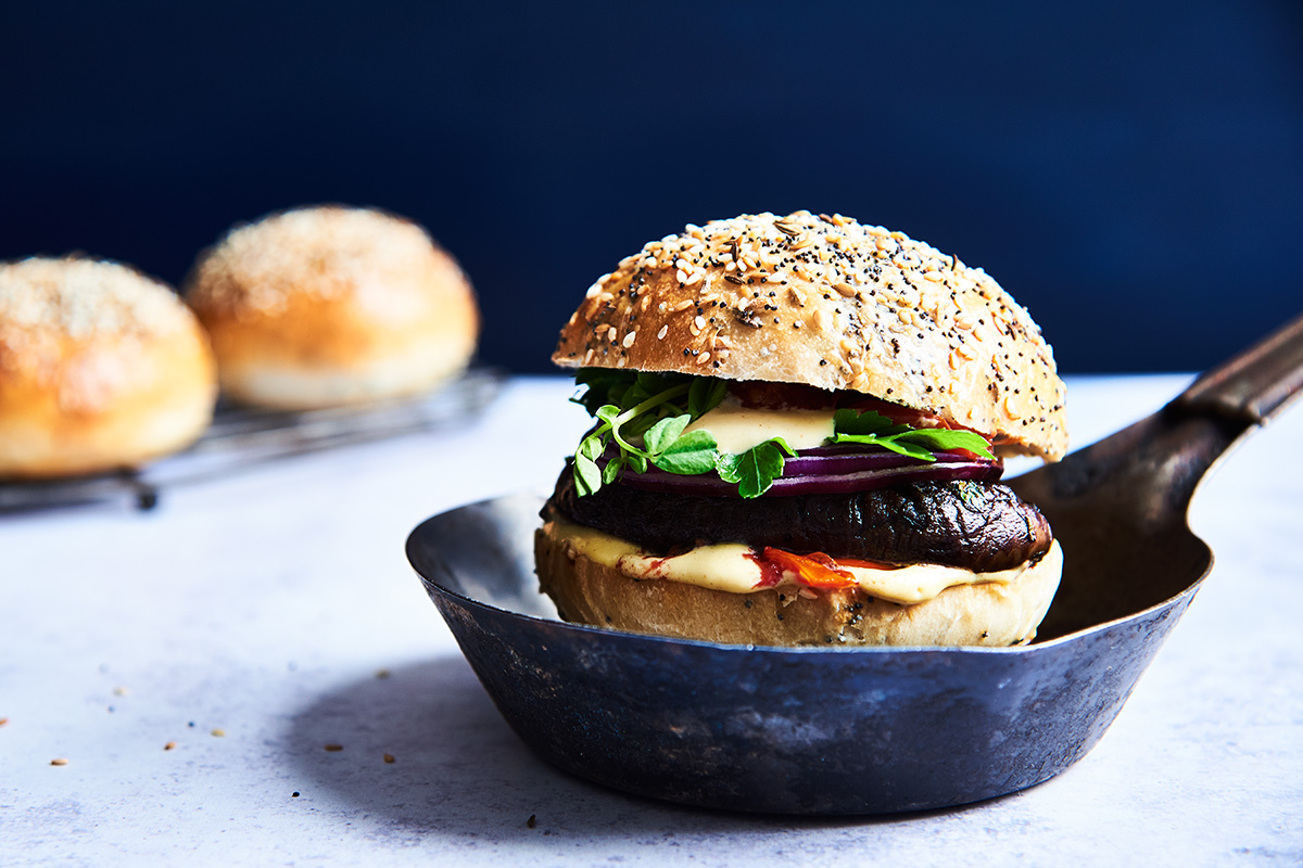 A portobello mushroom on a homemade hamburger bun in a cast iron pan with a few burger buns in the background