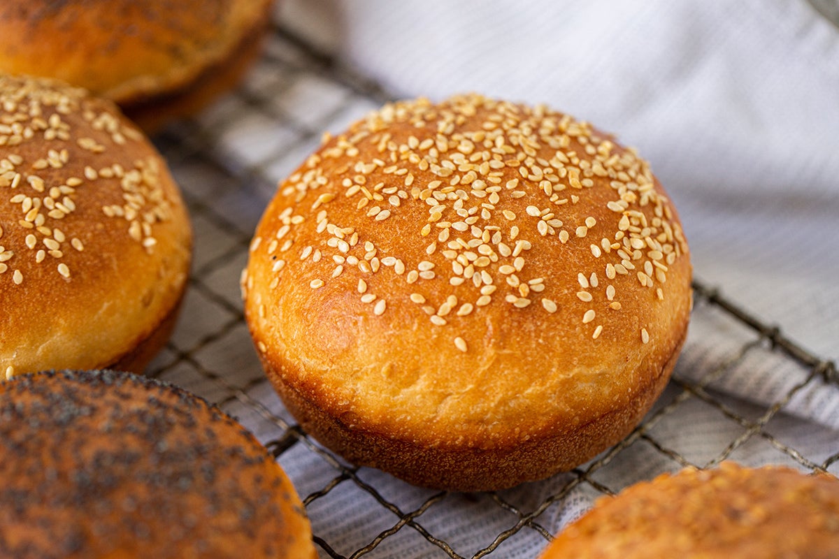 Homemade hamburger buns with a variety of toppings cooling on a rack