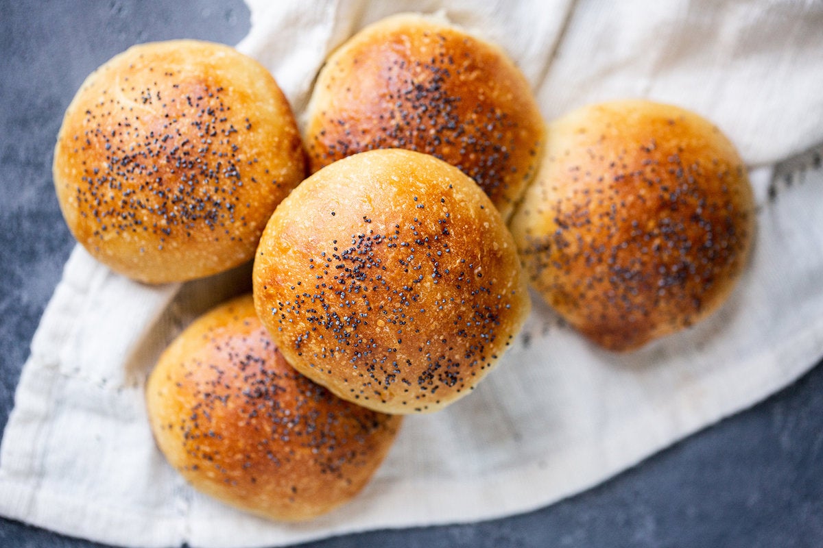 Bollos de hamburguesa caseros cubiertos con semillas de amapola en un paño de cocina