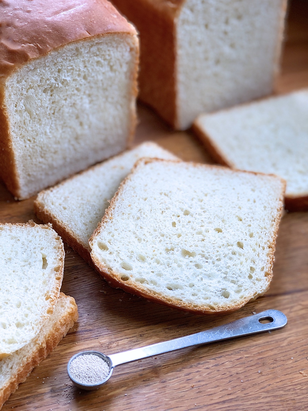 Half-teaspoon of yeast in front of three loaves of sliced bread.