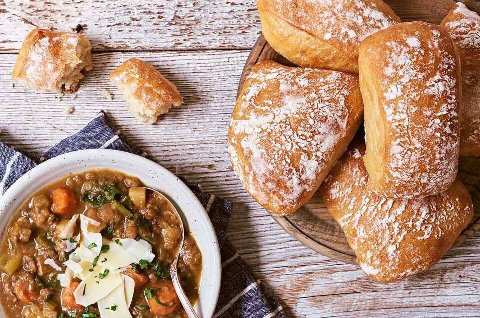 Chewy Italian Rolls on a serving board with a bowl of soup.