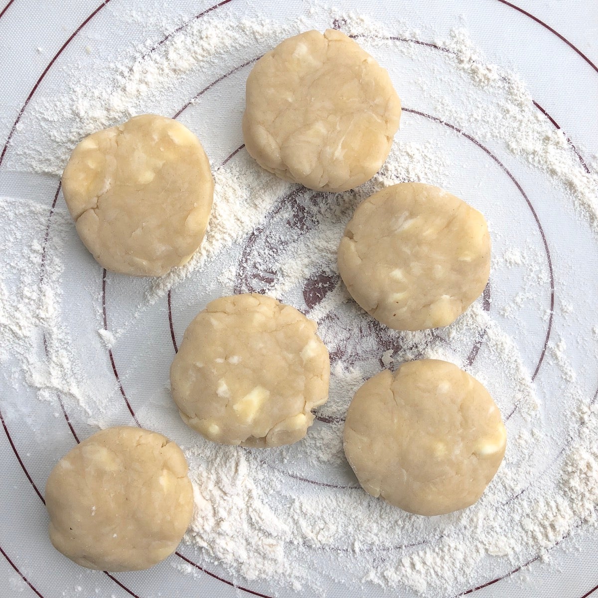 Six 2"-wide discs of pie pastry on a floured silicone mat.