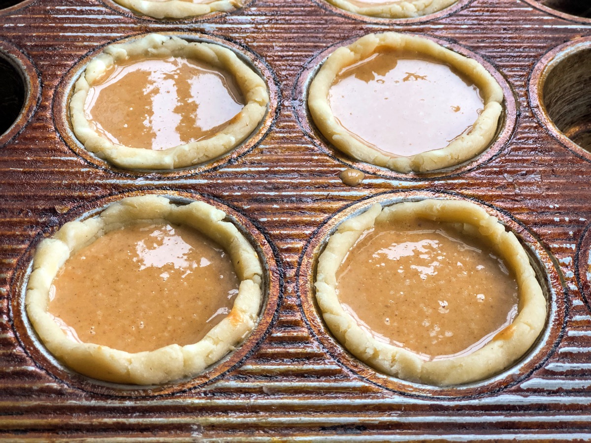 Mini pie crusts with pumpkin filling, showing filling coming almost to the top of the crusts.