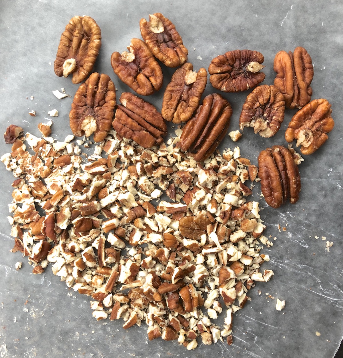 Diced pecans and pecan halves on a piece of waxed paper.