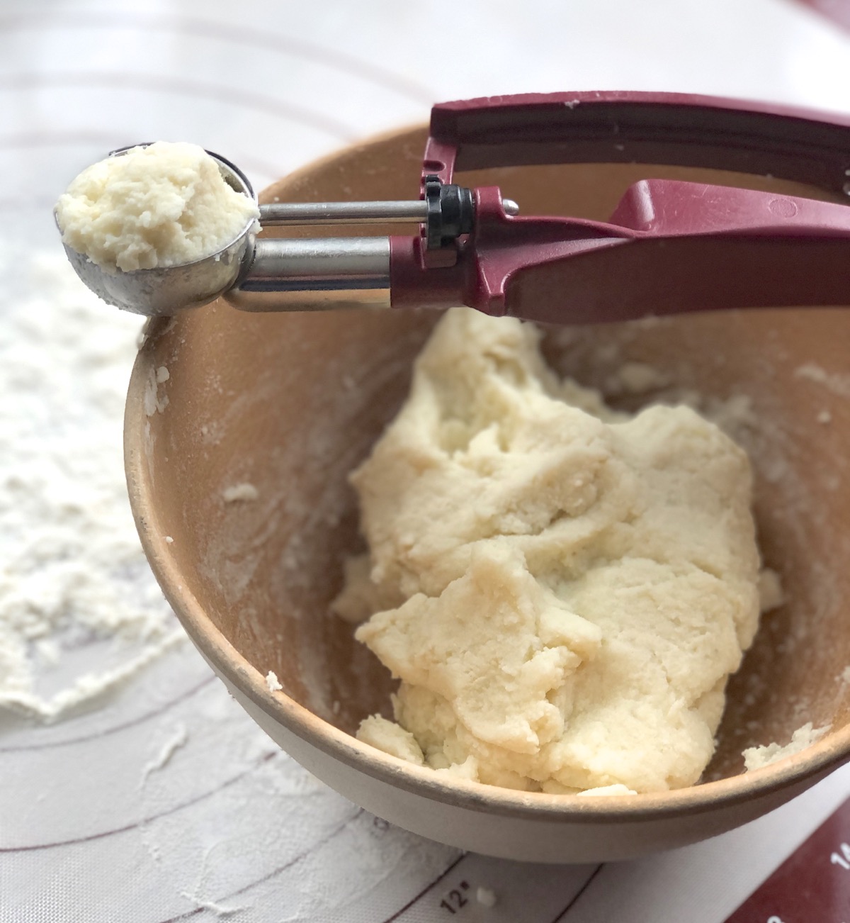 Lefse dough in a bowl, tablespoon cookie scoop holding a generous scoop alongside.