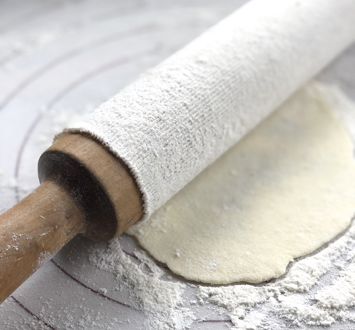 Wooden rolling pin with a cotton cover atop a rolled-out round of lefse dough.