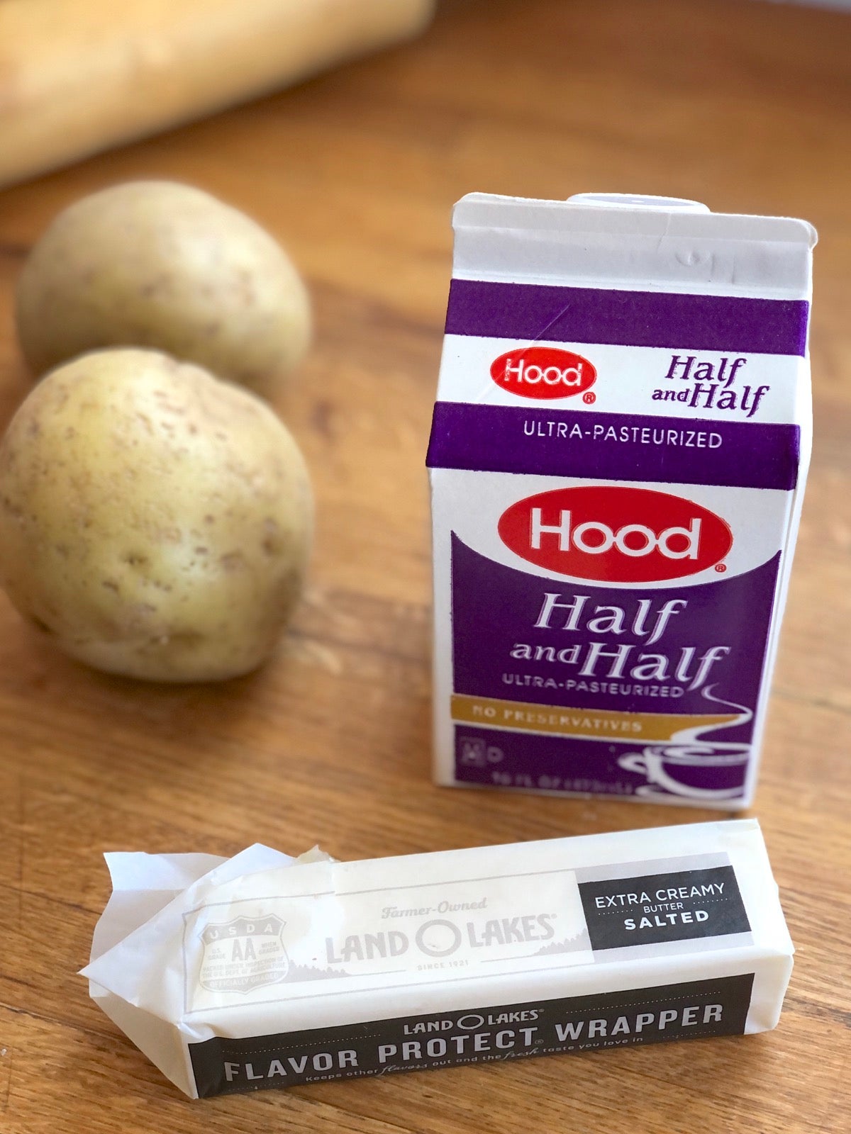 Stick of butter and carton of half and half on a wooden tabletop.