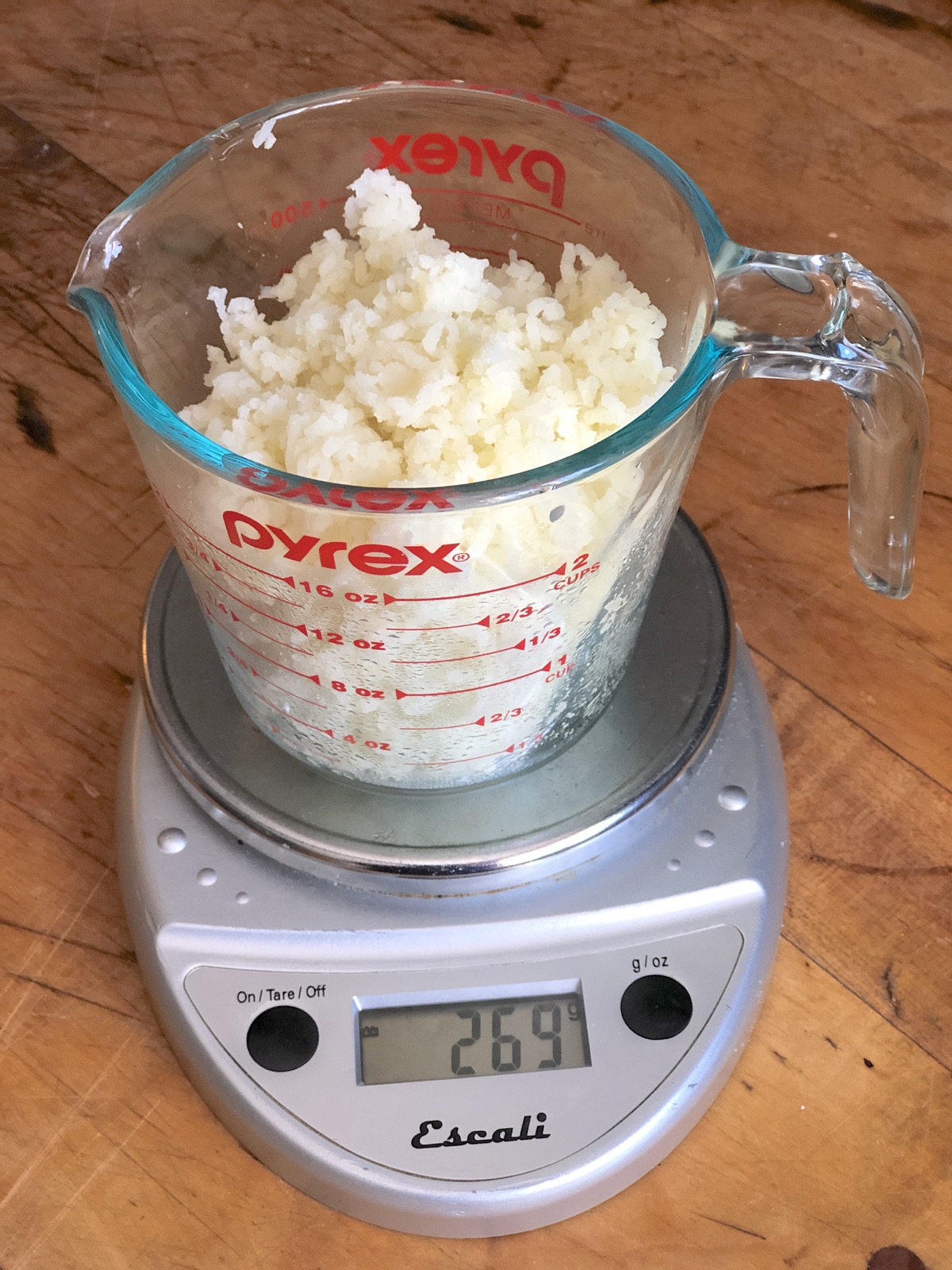 Riced potatoes in a measuring cup set on a scale.