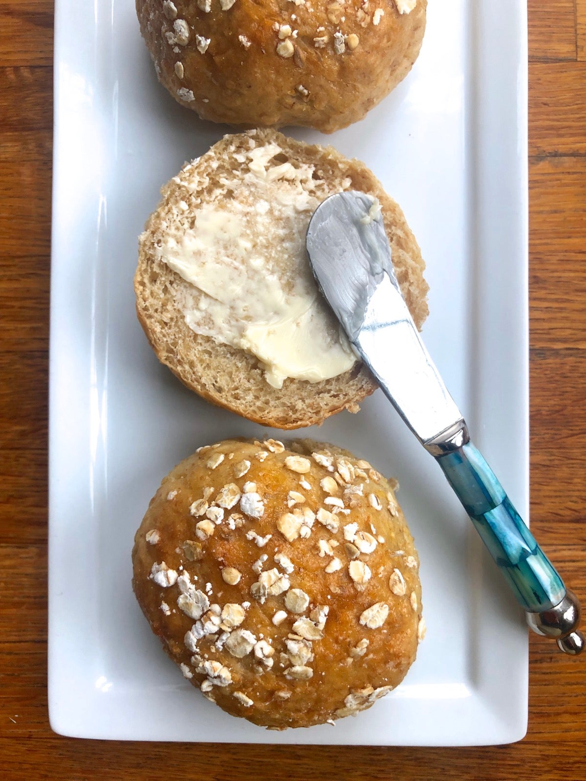 Whole grain dinner rolls on a plate, one split open and buttered.