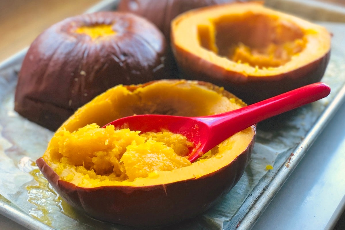 Baked pumpkin halves on a baking sheet, pulp being scooped from one