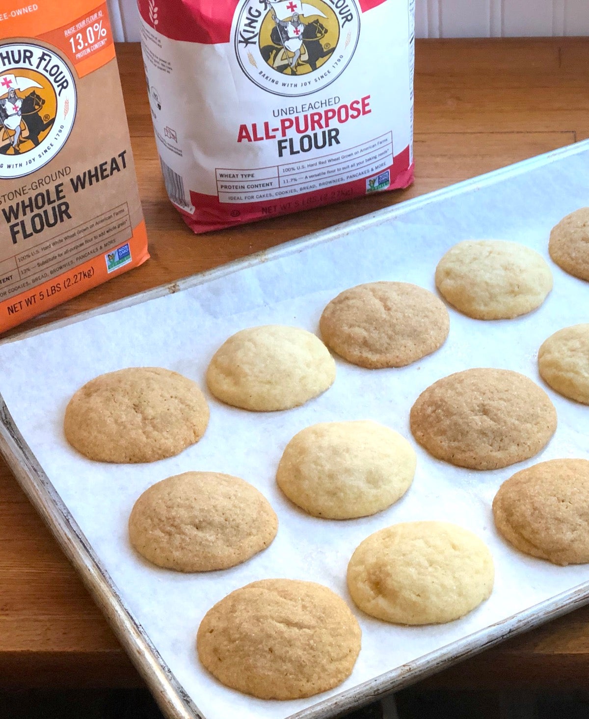 Sugar cookies n a baking sheet, half made with whole wheat flour, half with all-purpose flour.