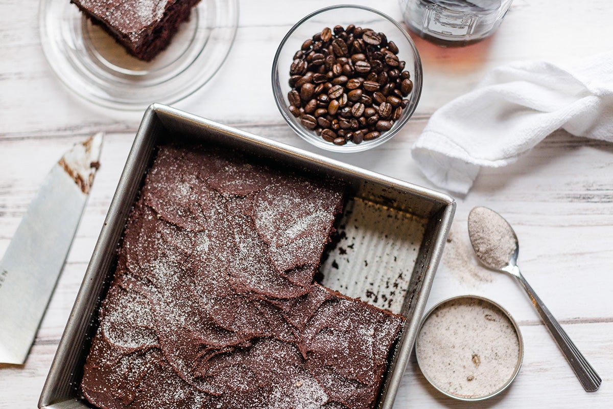 A chocolate cake topped with coffee sugar next to a cup of coffee and a slice of cake